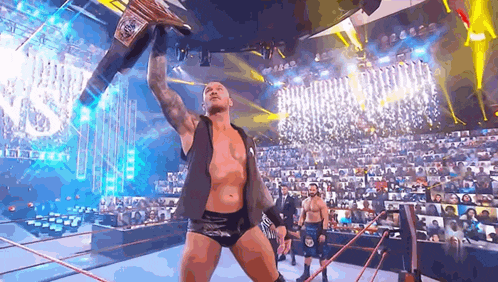 a wrestler is holding a championship belt in the air while standing in a wrestling ring .