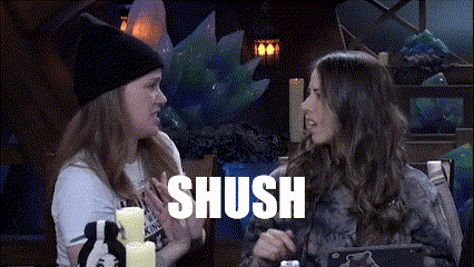 two women are sitting at a table and one of them is saying shush .