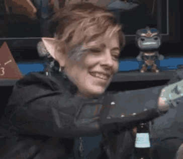 a woman with elf ears is laughing and holding a bottle of beer .