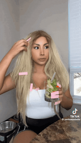 a woman with long blonde hair is holding a glass with a straw and sticky notes in her hair