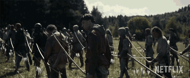 a group of people holding bows and arrows in a field with a netflix logo in the corner
