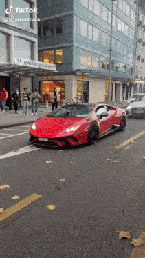 a red lamborghini is driving down a street in front of a building that says tiktok