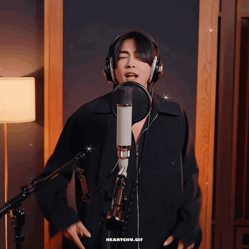 a man wearing headphones is singing into a microphone with the gif heartchu.gif below him