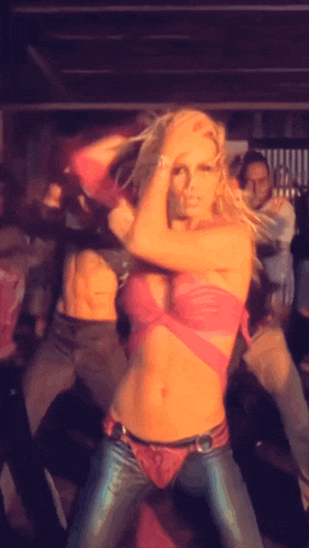 a woman in a pink top and blue jeans is dancing in a crowd
