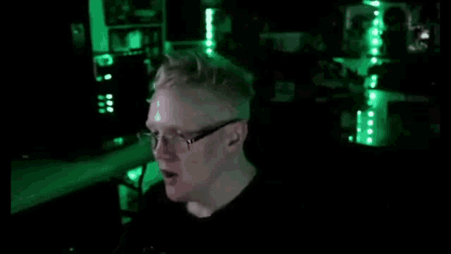 a man wearing glasses is sitting in front of a computer monitor in a dark room .