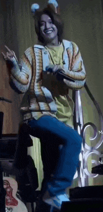 a man in a sweater is standing on a stage holding a microphone and smiling .