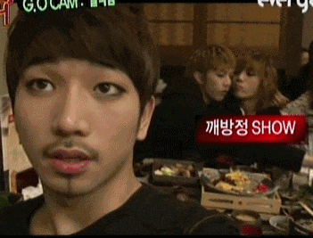 a man with a beard looks at the camera with a red sign that says show