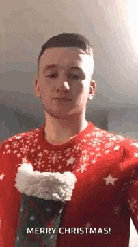 a young man in a red sweater is holding a christmas stocking and wishing merry christmas .