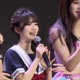 a girl is holding a microphone and smiling while standing next to another girl .