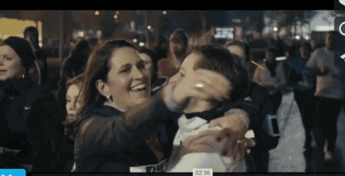a woman is hugging a child in front of a crowd with the time of 02:36