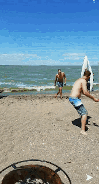 two men are playing frisbee on a beach near the ocean