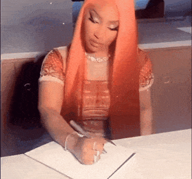 a woman with pink hair is sitting at a table writing in a notebook .