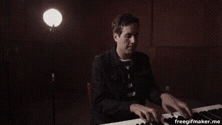 a man is playing a piano in a dark room with a light behind him .