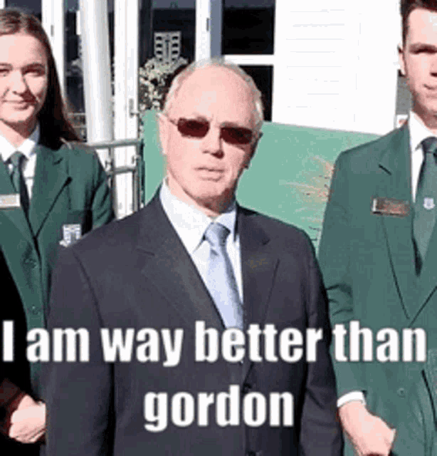 a man in a suit and tie stands in front of a group of people with the caption i am way better than gordon .
