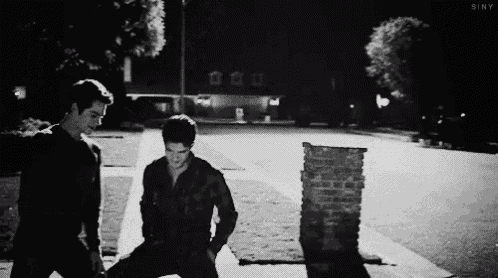 two men are standing next to each other on the sidewalk at night .