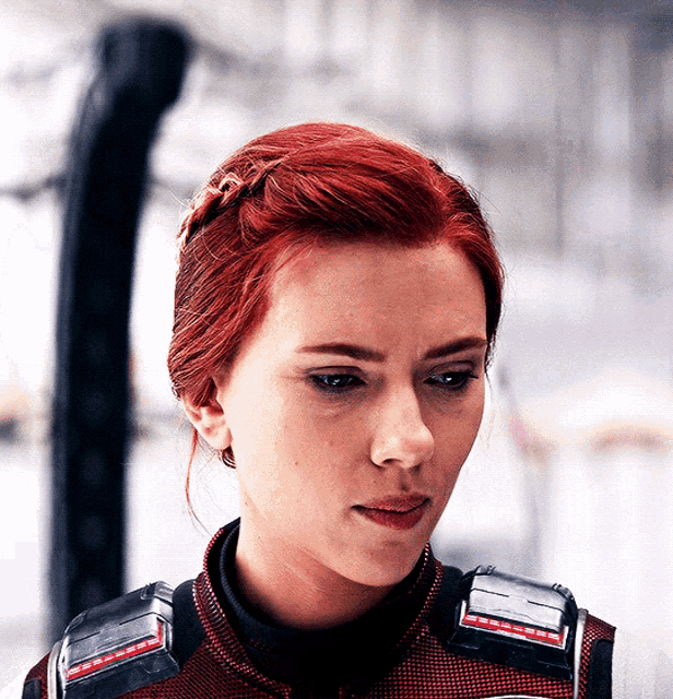a close up of a woman 's face with red hair wearing a black and red jacket