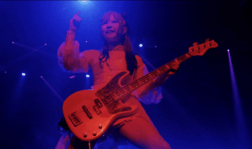 a woman is playing a bass guitar on a stage with blue lights behind her
