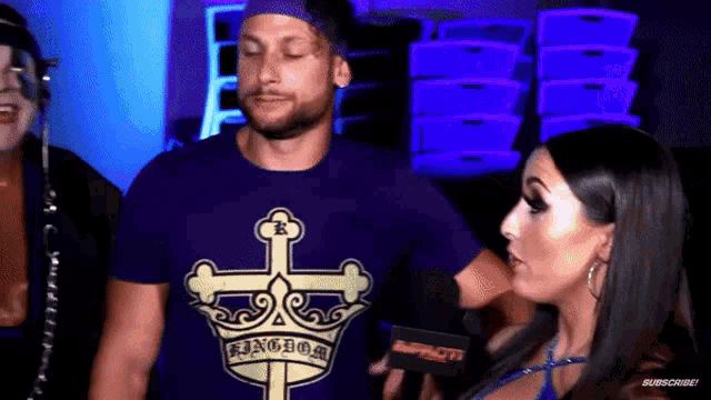 a man wearing a purple shirt with a cross and crown on it is being interviewed by a woman .