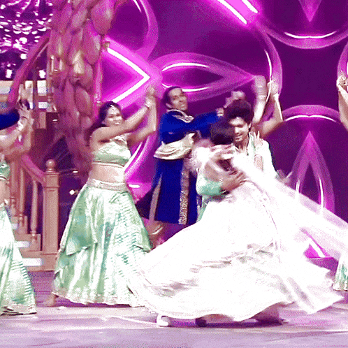 a group of people are dancing on a stage with purple lights in the background