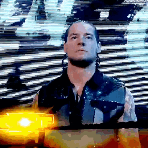 a wrestler is standing in front of a large screen with a yellow light behind him .