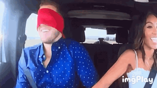 a man wearing a blindfold is holding a woman 's hand in a car