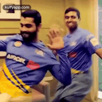 two men are dancing together in a room while wearing blue shirts and yellow shorts .
