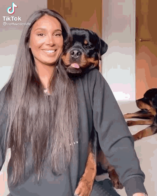 a woman is holding a rottweiler dog on her shoulder and the dog is sticking out its tongue
