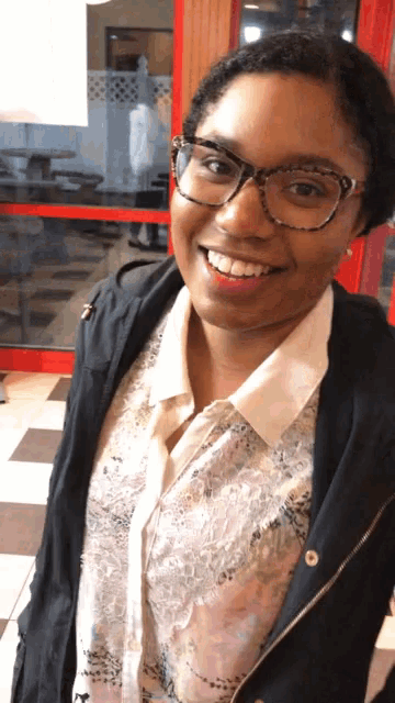 a woman wearing glasses and a black jacket smiles at the camera