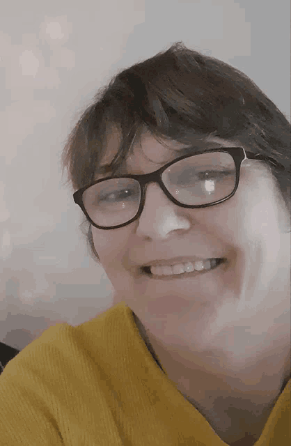 a woman wearing glasses and a yellow sweater smiles