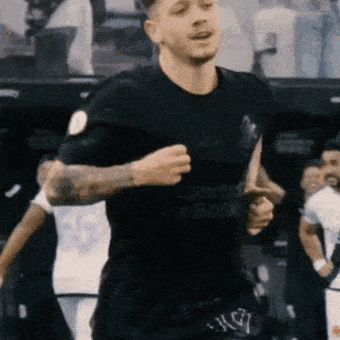 a man in a black adidas shirt is running on a field .
