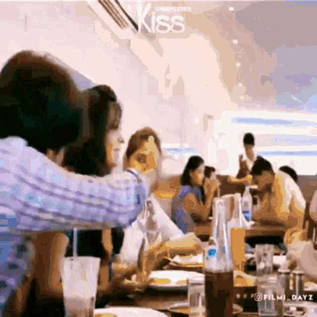 a group of people are sitting at tables in a restaurant with a sign that says kiss on it .