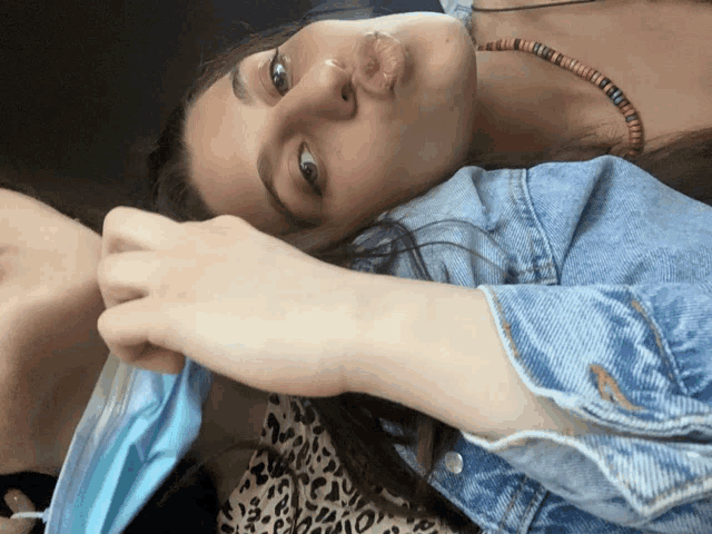 a woman wearing a denim jacket is laying next to another woman wearing a mask