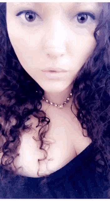a close up of a woman 's face with curly hair and a necklace .