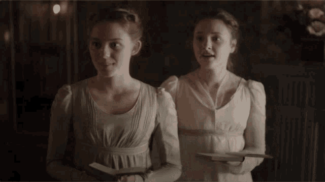 two women in white dresses are standing next to each other holding books