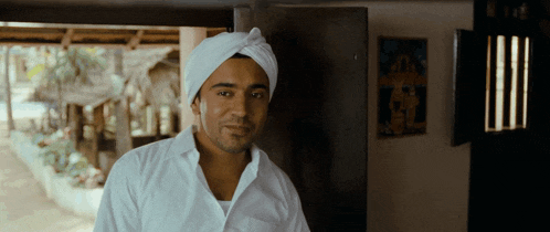 a man wearing a white shirt and a turban is standing in front of a door