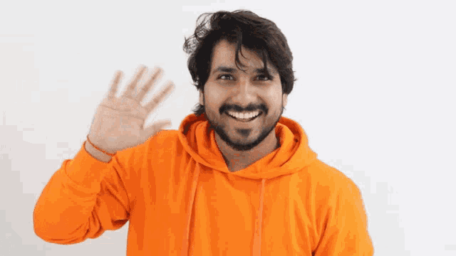 a man wearing an orange hoodie is smiling and waving his hand