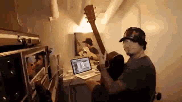 a man is playing a guitar while sitting at a desk with a laptop .