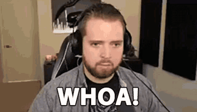 a man with a beard wearing headphones is sitting in front of a microphone and saying whoa .