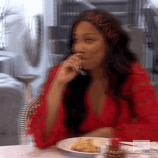 a woman in a red dress is sitting at a table with a plate of food and a bravo logo on the bottom