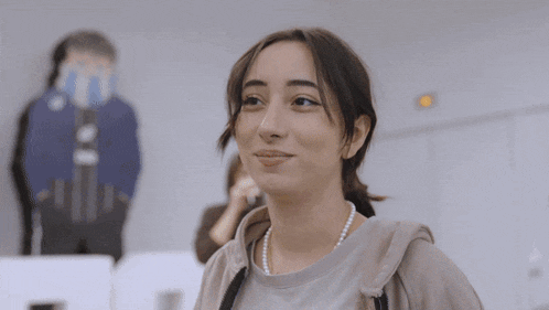 a woman wearing a pearl necklace and a hoodie smiles