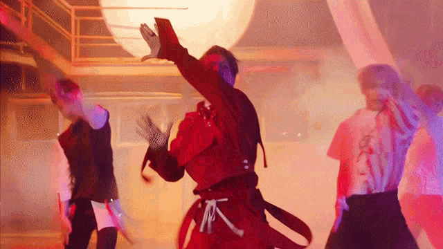 a group of people are dancing on a stage in a dark room with smoke coming out of the ceiling .
