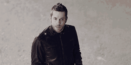 a man in a black leather jacket is standing on a sandy beach .