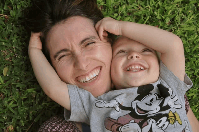 a woman and a child are laying in the grass and the child is wearing a mickey mouse shirt