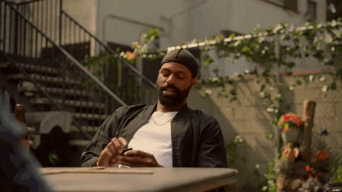 a man with a beard is sitting at a table using a cell phone .