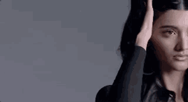 a woman is touching her hair with her hand while looking at the camera .