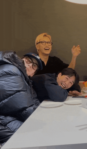three people sitting at a table with one wearing glasses and a hat