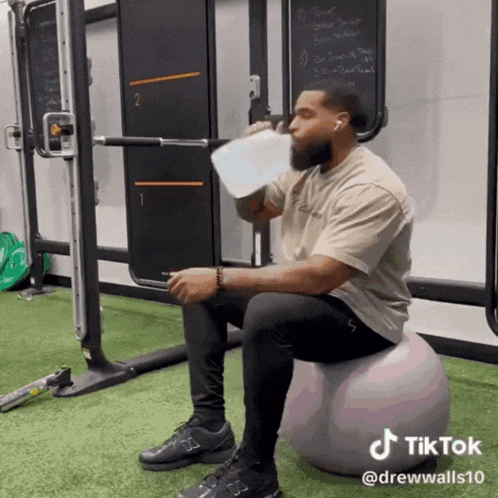 a man is drinking water while sitting on a ball with a tiktok watermark