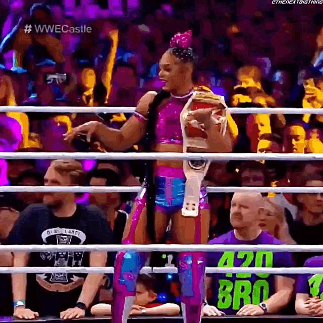 a woman is standing in a ring holding a wrestling championship belt .