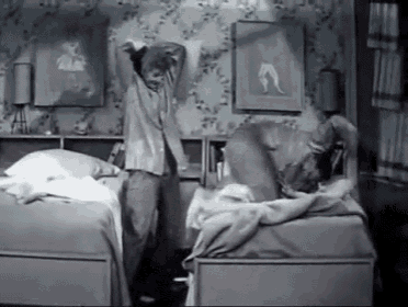 a black and white photo of a man standing in a bedroom next to two beds .