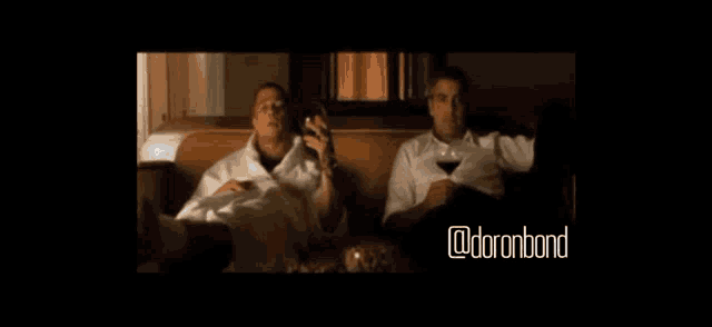 two men are sitting on a couch drinking wine and reading a book with the words @doronbond below them